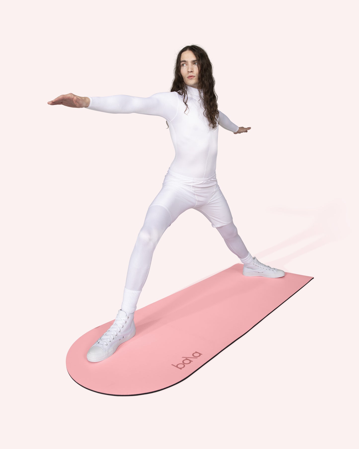 ine Person mit langen Haaren macht eine Yoga- oder Fitnessübung auf einer rosafarbenen Bala Play Mat.